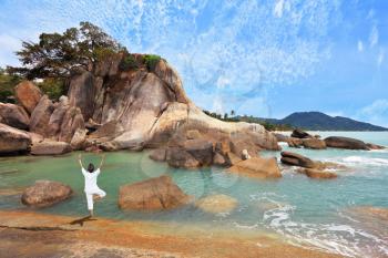 Gorgeous beach on the Andaman Sea. Middle-aged woman dressed in white doing yoga. 
Pose Tree, stand on one leg
