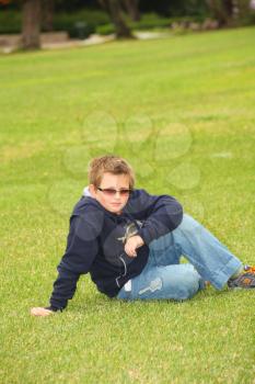 The beautiful boy in protective solar glasses has a rest on a green lawn in park