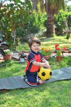 A little boy with a charming smile, poses on a green lawn. He carried a yellow ball
