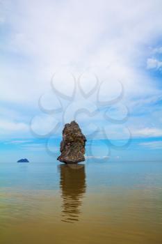 The haze of the warm sea - background for the huge stone cliff. Island Sail in the ocean. The island is reflected in the smooth surface of the water
