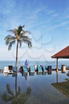 The luxurious marble pool on the island of Koh Samui. Palm tree and beach chairs are reflected in the smooth surface of the water