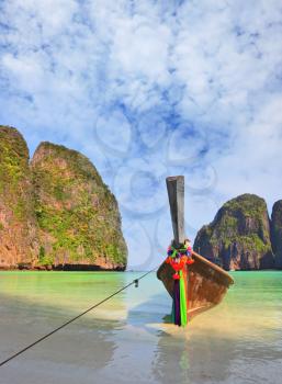 Picturesque green islands of the Thai coast. Emerald sea and thin white sand. On a beach the tourist boat decorated with a red silk scarf is moored