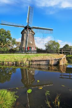 Rural landscape in the Netherlands. Verdant grove, quiet stream and a symbol of the country - Windmills