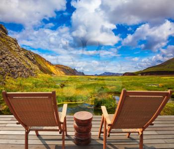 Two comfortable wooden chairs and small table stand for tired tourists.  Volcanic summer tundra. Travel to Iceland in July