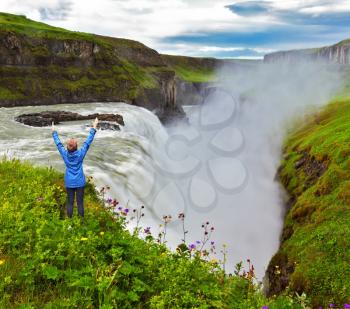 Powerful Gullfoss in Iceland. On the hillside woman thrilled looking at the boiling abyss