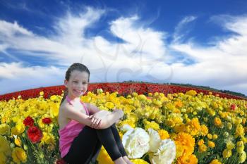 Charming smiling girl with a scythe in the kibbutz field of blooming yellow and red buttercups