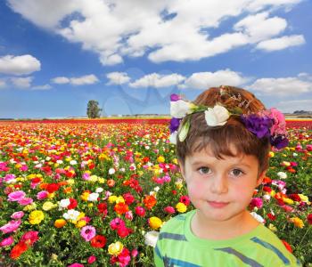 The charming little boy in flower garland on the background of colorful flower fields