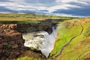 Grand Gullfoss in Iceland. Summer sunny day. Roaring water lit by the morning sun. The river banks are overgrown with green moss northern