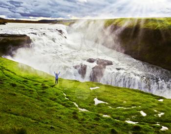 On the hillside woman thrilled looking at the boiling abyss. Powerful Gullfoss in Iceland. 