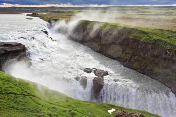 Roaring water glistens on the northern sun. Fantastically spectacular cascading waterfall Gyullfoss. Iceland in the summer