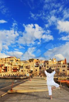 Fishing jetty port,  the woman in white performs asana Tree on one leg. Sunset over the Old Jaffa in Tel Aviv