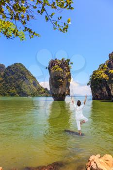 Exotic vacation in Thailand. Woman performs yoga pose standing in the water of the Andaman Sea