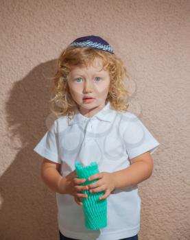 Adorable Jewish child in a blue  skullcap - yarmulke. Little boy with long blond curls and blue eyes