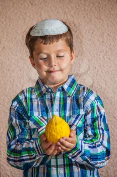  Etrog -  ritual fruit for the Jewish holiday of Sukkot. Beautiful seven year old boy in white knitted skullcap is holding citron