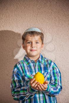 The etrog - ritual fruit for Jewish holiday of Sukkot. The charming seven-year-old boy in white festive skullcap holds citrus in hand