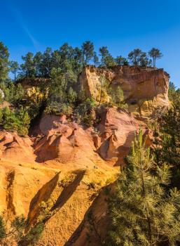 Multi-colored outcrops - from yellow to red-orange. Roussillon, Red village of Provence. Green trees create beautiful contrast from ochre