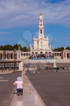 FATIMA, PORTUGAL - SEPTEMBER 9, 2011: The religious woman in hat is kneeling specially constructed path. The square in front of a Catholic cathedral with tourists and believers