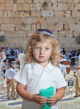 The Jewish holiday of Sukkot. Adorable little boy with long blond curls and blue eyes in  knitted skullcap. He stands at main Jewish shrine - the Western Wall of Temple