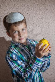 Very beautiful seven year old boy in white knitted kippah is holding citrus.  Etrog  -  ritual fruit for Sukkot