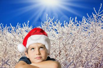 Very beautiful seven year old boy in red hat of Santa-Claus smiling  on the background of the winter forest