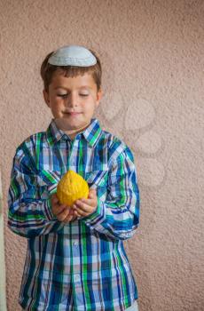  Etrog -  ritual fruit for the Jewish holiday of Sukkot. Beautiful seven year old boy in white knitted skullcap is holding citrus