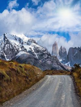 Legendary rocks Torres is surrounded by snow-capped black rocks. These leads dirt road. National Park Torres del Paine. Travel in Chile. The concept of active and extreme tourism