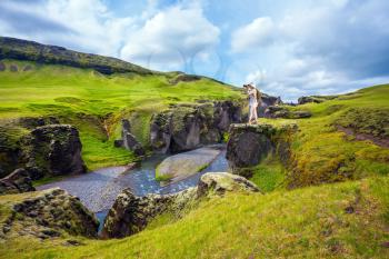 The elderly woman standing on a rock and photographing the scenic landscape. The striking canyon Fyadrarglyufur in Iceland. Green Tundra in summer. The concept of active northern tourism