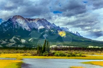Impressive trip to the Rocky Mountains of Canada. Rocks, lakes and yellow grass under flying clouds. Concept of active automobile and ecological tourism