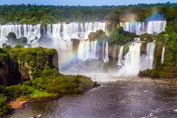 Powerful waterfall creates a watery dust and a rainbow. Several waterfalls from 275 Iguazu Falls. The concept of exotic and extreme tourism