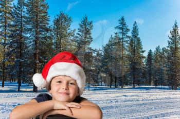 New Years is soon. A handsome boy in a red Santa Claus hat is smiling. Winter forest in the snow