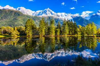 Concept of active and ecotourism. Mountain resort of Chamonix, the foot of Mont Blanc. Fantastic sunset in the autumnal Alps. Stunning reflections of snowy peaks in the lake water