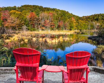 Magnificent resort in French Canada - Mont Tremblant. Red plastic loungers on the shore of the pond. Foliage of forests is reflected in the pond. Concept of ecological tourism