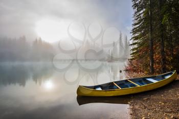 The sun peeps through the mist. Fishing boats moored on the shore. Emerald Lake in Yoho National Park