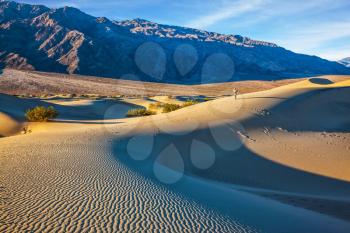 Small sandy ripples on orange barkhans. Mesquite Flat Sand Dunes in California. Woman in straw hat  photographing sand waves