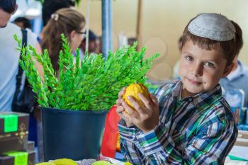 Holiday market in Jerusalem. Seven year old boy in white skullcap with etrog. Ritual plants - myrtle prepared for sale


