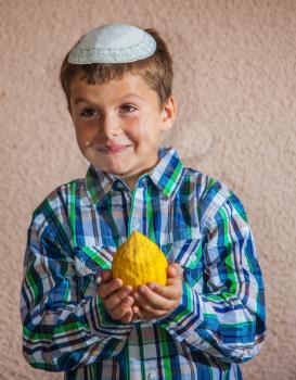  Citron - ritual fruit for the Jewish holiday of Sukkot. Beautiful seven year old boy in white knitted skullcap is holding citrus