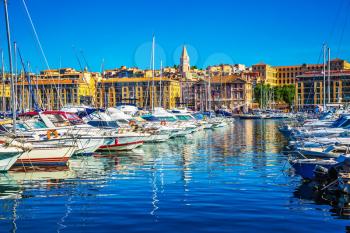 The blue water reflects the ancient buildings on the waterfront. Rows of sailing yachts, motor boats and fishing boats. The water area of Marseille Old Port