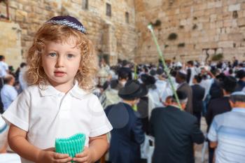 Beauteous little boy with blue eyes and blond side curls, in skullcap. Autumn Jewish holiday Sukkot.  The greatest shrine of Judaism is the Western Wall of the Temple