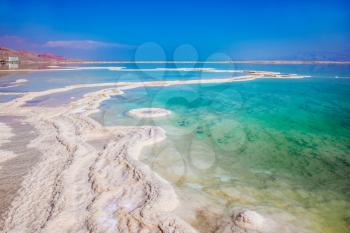 Very salty water glows with turquoise light. Reduced water in the Dead Sea. The concept of ecological and medical tourism. The evaporated salt has developed into fantastic patterns