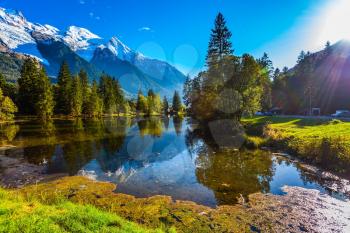 The lake reflects the forest and the blue sky. Chamonix City Park is illuminated by sunset. Sunny autumn day in the French Alps. Concept of active winter tourism