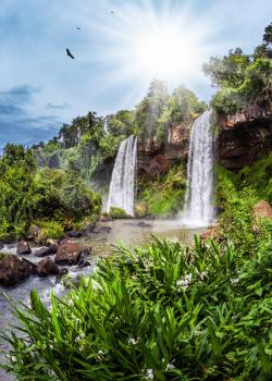 Two waterfalls from the Iguazu Falls in Argentina. Hot tropical sun illuminates the rumbling waterfalls. The concept of extreme and ecological tourism