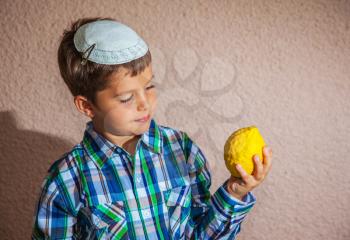 Very beautiful seven year old boy in  white knitted kippah is holding citrus. Citrus -  ritual fruit for Sukkot