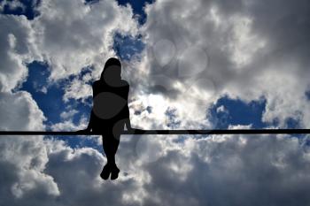 Girl silhouette sitting against cloudy sky background; peace concept