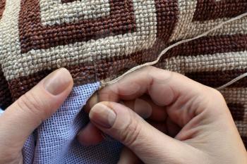 Hands of woman embroidering traditional pattern with geometric motifs
