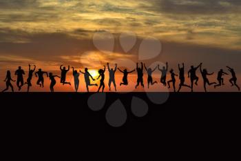 Happy men and women silhouettes jumping at sunrise