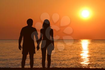 Young couple holding hands watching a sunrise at seashore