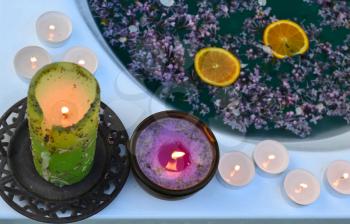 Colored candles on the edge of the bathtub full with blue water and lilacs flowers