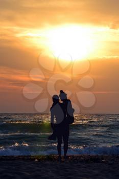 Silhouette of man carrying woman in his arms on the beach at sunset