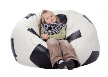 Girl with long blonde hair sitting on an inflatable chair in the form of a soccer ball, isolated on a white background