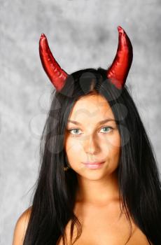 halloween style - portrait of sexy brunette with red horns on grey
